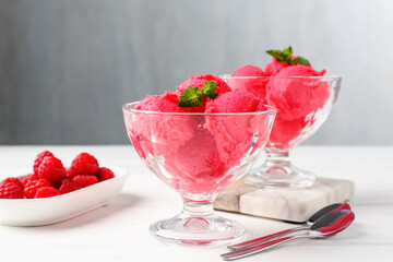 Delicious raspberry sorbet with mint in dessert bowls, spoons and fresh berries on white wooden...