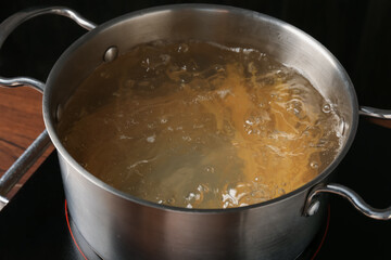 Fresh tagliatelle pasta boiling in pot with water on electric stove, closeup
