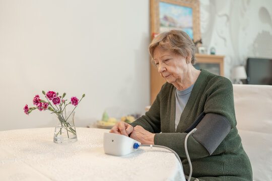 Senior woman measures her blood pressure while sitting at home in comfortable environment. Concept of health, wellness, self-care, medical monitoring, and senior independence. Healthcare for seniors.