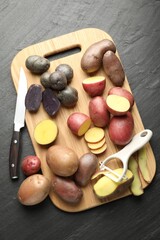 Different types of potatoes, peeler and knife on black table, flat lay