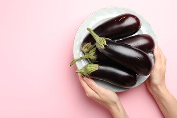 Woman with plate of fresh eggplants on pink background, top view. Space for text
