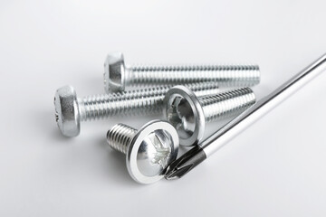 Different metal bolts and screwdriver on light background, closeup