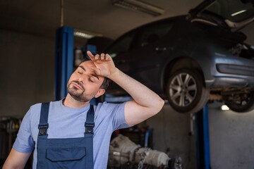 Exhausted mechanic wiping sweat from forehead in auto repair shop