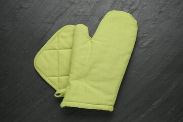 Green oven glove and potholder on dark textured table, top view