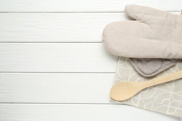 Oven glove, potholder, spoon and towel on white wooden table, top view. Space for text