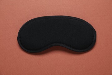 Sleeping mask on brown background, top view