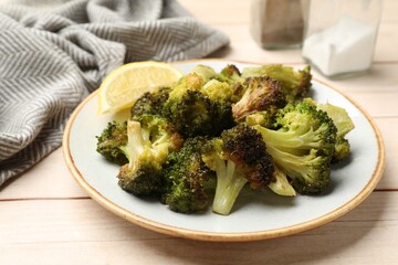 Tasty fried broccoli and lemon on light wooden table, closeup