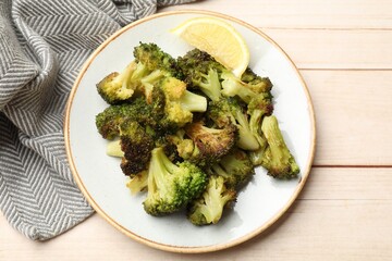 Tasty fried broccoli and lemon on light wooden table, top view