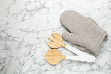 Oven glove, potholder and other kitchen utensils on white marble table, flat lay. Space for text
