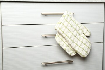 Oven glove and potholder hanging on handle of cabinet in kitchen
