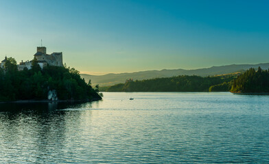 Evening view of Niedzica Castle silhouetted against the fading sky. Seagulls rest on the riverside...