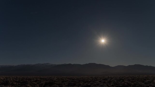 Moonset behind panamint mountains as sun rises over devils golfcourse in death valley on a dusty winter day