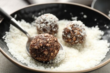 Making tasty chocolate candies with nuts and coconut flakes at light table, closeup