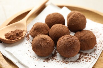 Tasty chocolate candies with cocoa powder and spoon on light table, closeup