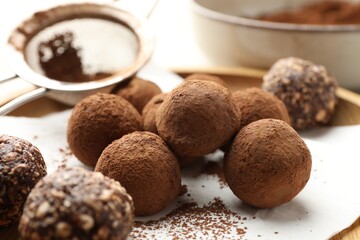 Tasty chocolate candies with cocoa powder and strainer on light table, closeup