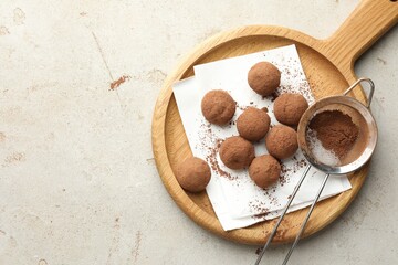 Tasty chocolate candies with cocoa powder and strainer on light table, top view. Space for text