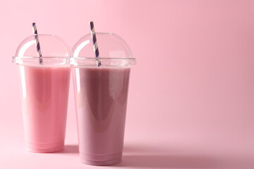 Tasty milkshakes in plastic cups on pink background, space for text