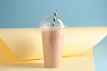 Tasty milkshake in plastic cup on color background
