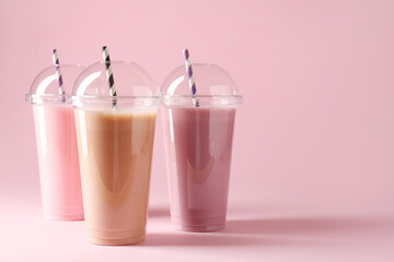 Tasty milkshakes in plastic cups on pink background, space for text