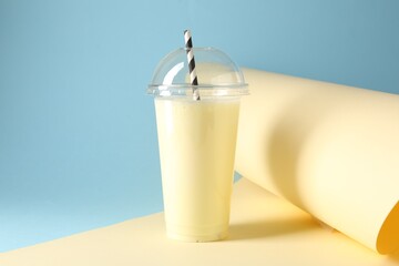 Tasty milkshake in plastic cup on color background