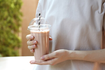 Woman holding tasty milkshake in plastic cup outdoors, closeup
