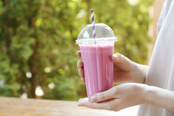 Woman holding tasty milkshake in plastic cup outdoors, closeup