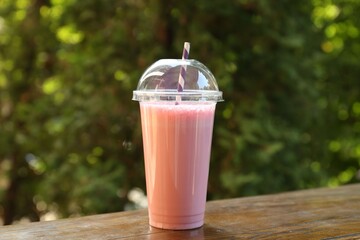 Tasty milkshake in plastic cup on wooden table outdoors