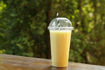 Tasty milkshake in plastic cup on wooden table outdoors
