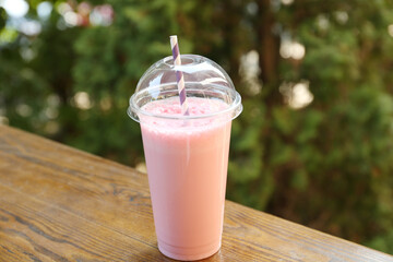 Tasty milkshake in plastic cup on wooden table outdoors