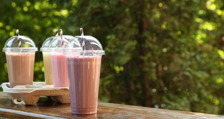 Tasty milkshakes in plastic cups on wooden table outdoors, space for text