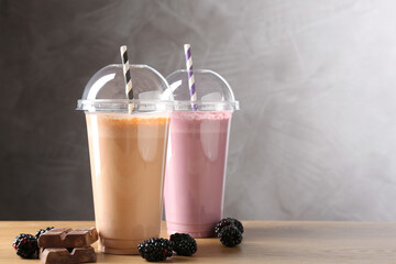 Tasty milkshakes in plastic cups and ingredients on wooden table, space for text