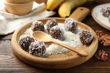 Tasty chocolate candies with nuts and coconut flakes on wooden table, closeup