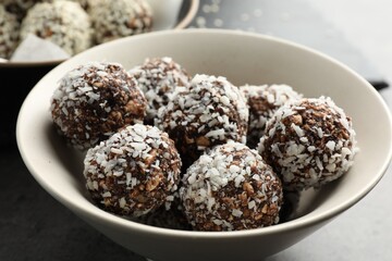Tasty chocolate candies with nuts and coconut flakes in bowl on table, closeup