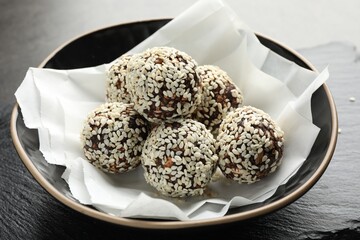 Tasty chocolate candies with nuts and sesame seeds in bowl on table, closeup