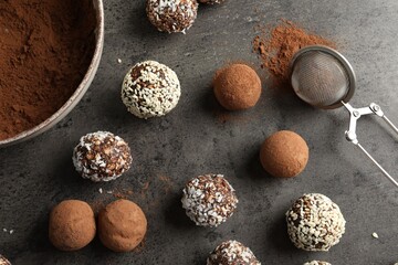 Tasty chocolate candies with cocoa powder, nuts, coconut flakes and sesame seeds on grey table,...