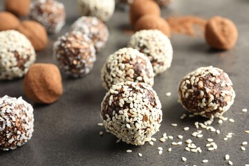Tasty chocolate candies with cocoa powder, nuts, coconut flakes and sesame seeds on grey table,...