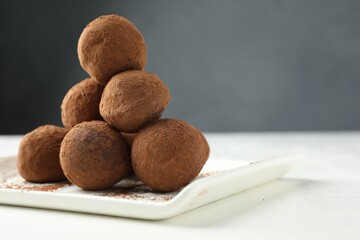 Tasty chocolate candies with cocoa powder on white table, closeup. Space for text