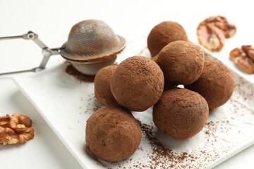 Tasty chocolate candies with cocoa powder and walnuts on white table, closeup