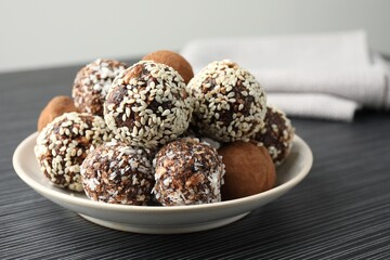 Tasty chocolate candies with cocoa powder, nuts and sesame seeds on black textured table, closeup