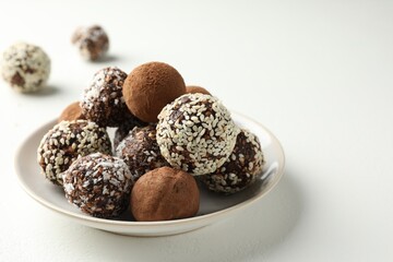 Tasty chocolate candies with cocoa powder, nuts and sesame seeds on white table, closeup. Space for text