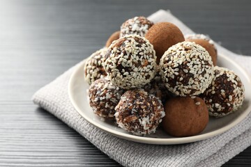 Tasty chocolate candies with cocoa powder, nuts and sesame seeds on black textured table, closeup