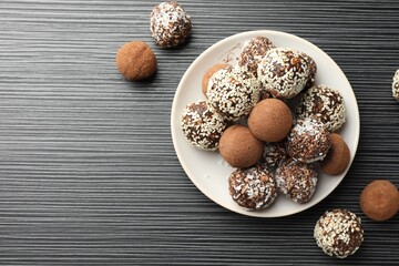 Tasty chocolate candies with cocoa powder, nuts and sesame seeds on black textured table, flat lay....