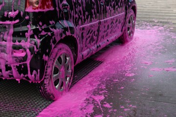 Auto covered with cleaning foam at outdoor car wash, closeup