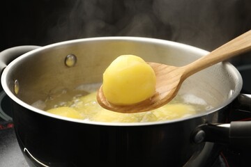Taking young potato out of boiling water at stove, closeup
