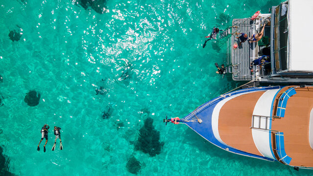 Aerial view of scuba divers swimming on water surface and climbing up on boat platform at Koh Racha Island, A destination for summer activity and scuba diving trip - Powered by Adobe