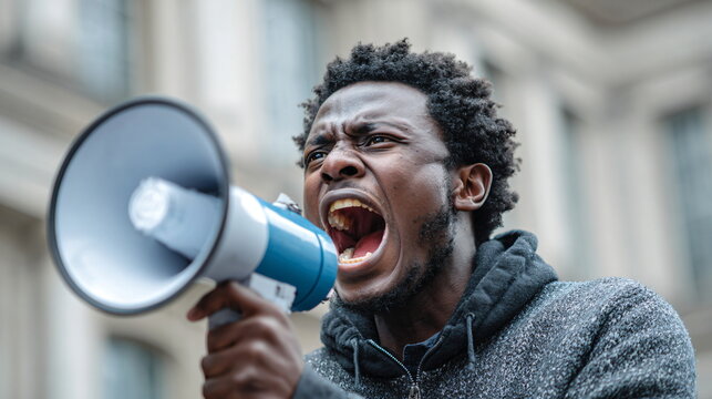 African american man using a megaphone, screaming and protesting outdoors. Street rally for activist issues during rain.