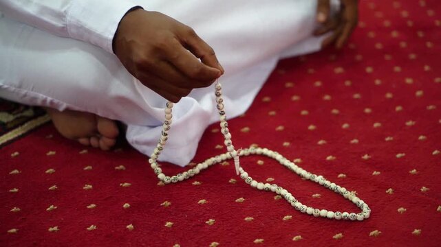 A man recites dhikr while holding prayer beads in his hand. Side view photo