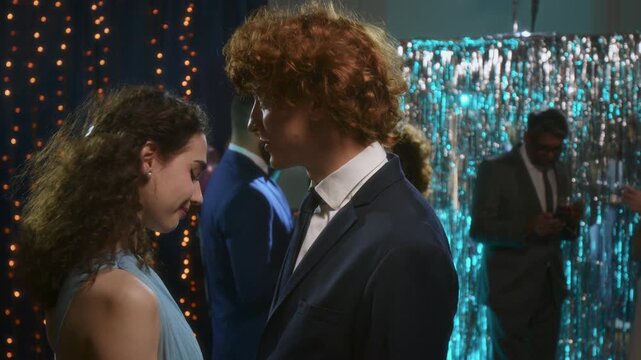 Young teenager couple in formal outfits laughing and talking while slow dancing at high school prom night