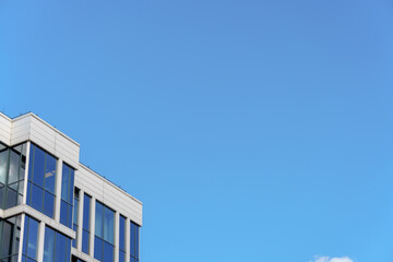  Top corner of a modern building with a white facade and large glass windows against a clear blue...