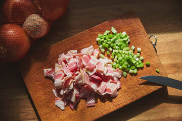 Top view of cutting board with chopped smoked bacon and spring onion, kitchen knife, onion mesh and...